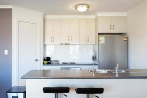 Eine moderne Küche mit weißen Schränken, einem Edelstahl-Kühlschrank, einem eingebauten Backofen und einer Bar mit zwei Hockern.