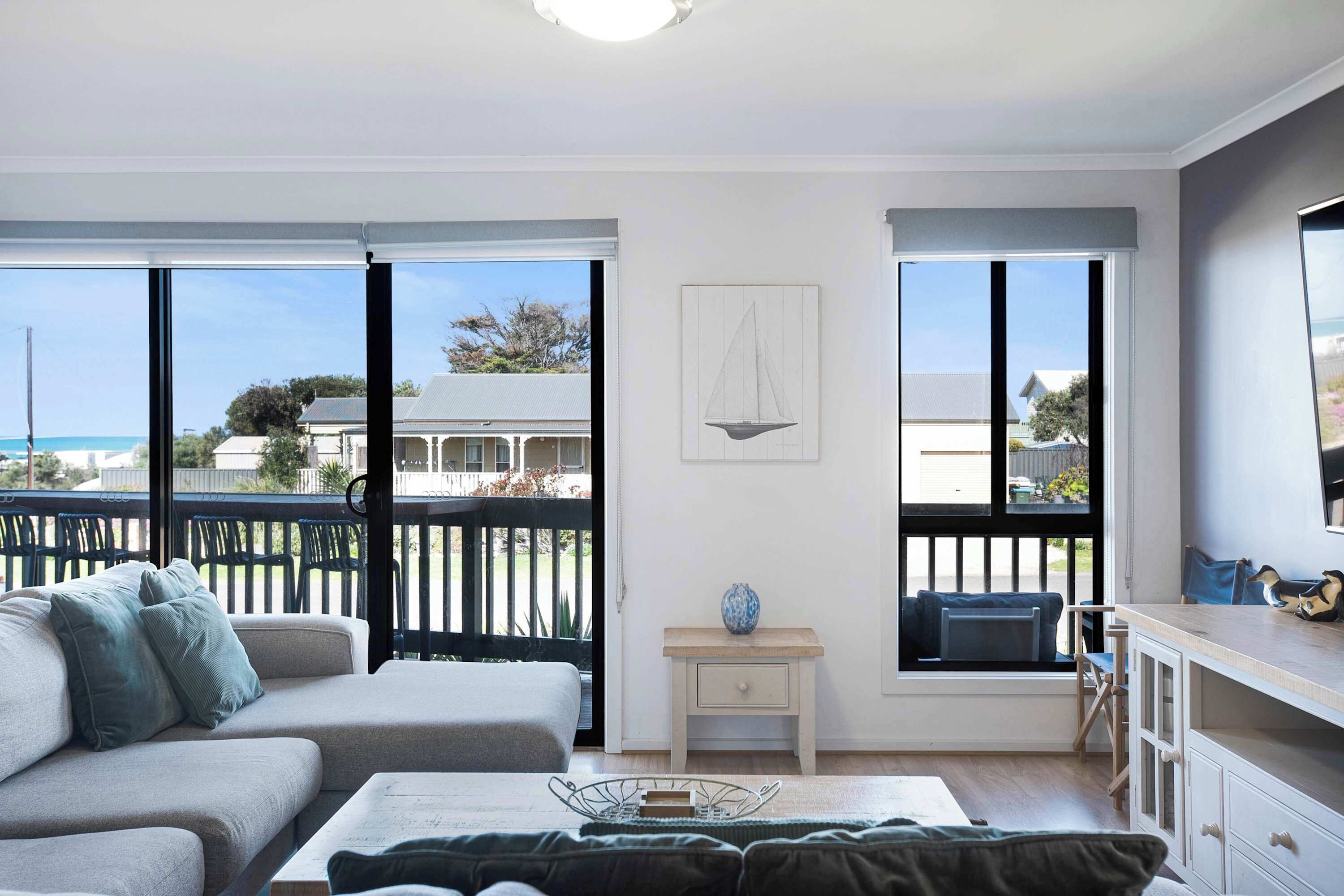 A modern living room with a sofa, a small table, and a view of the sea through large windows.