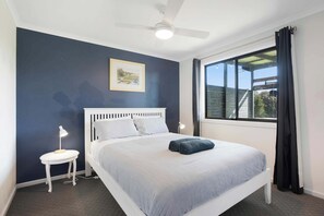 Ein Schlafzimmer mit einem Einzelbett, einem Deckenventilator, einem Fenster mit Vorhängen und einem kleinen Nachttisch mit Lampe.