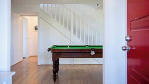 A room with a pool table, wooden flooring, a staircase, and a red door. - Morrison Shorehouse, Middleton Family Beach House (Middleton)