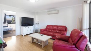 A living room with a flat-screen TV, a red leather sofa, a white coffee table, and a white cabinet. - Morrison Shorehouse, Middleton Family Beach House (Middleton)