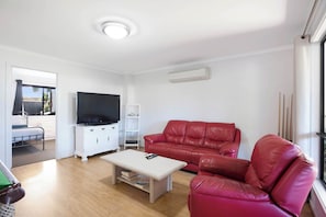 Ein Wohnzimmer mit Flachbildfernseher, einem roten Ledersofa, einem weißen Couchtisch und einem weißen Schrank.