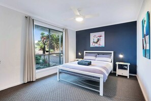 A bedroom with a bed, a ceiling fan, a window with curtains, a nightstand with a lamp, and a painting on the wall. - Morrison Shorehouse, Middleton Family Beach House (Middleton)