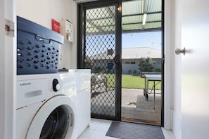 A laundry area with a Samsung washing machine, a blue laundry basket, and a door leading to an outdoor patio. - Morrison Shorehouse, Middleton Family Beach House (Middleton)