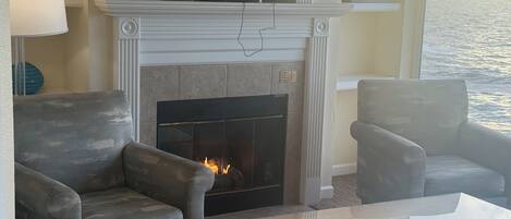 Una sala de estar con chimenea, un televisor de pantalla plana montado encima, dos sillones y una mesa de centro de vidrio.