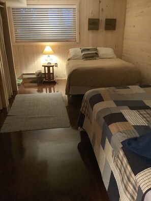 Ein Zimmer mit zwei Betten, einem Nachttisch, einer Lampe und einem Fenster mit Jalousien.