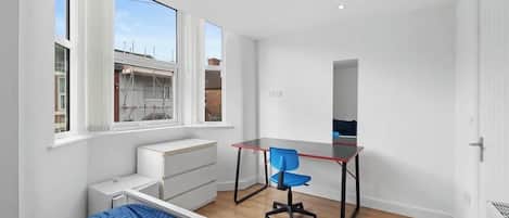 A bedroom with a bed, a desk, and a chair. There are windows and a door.