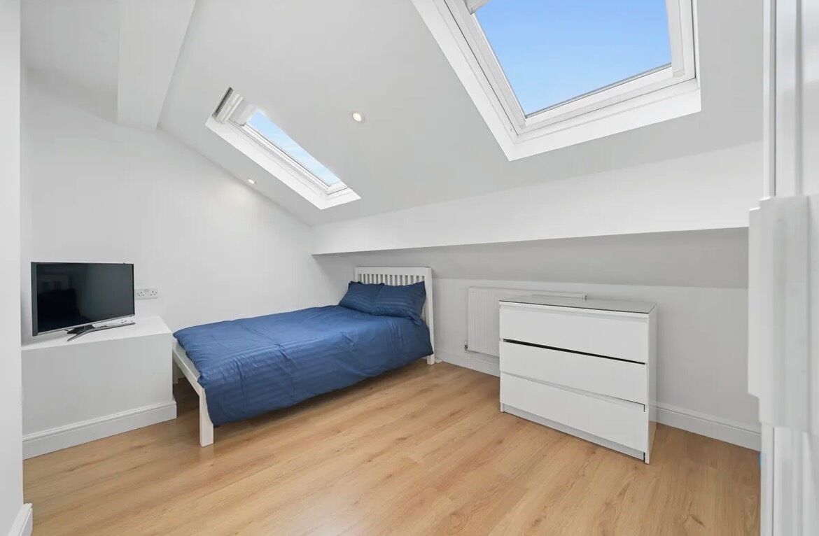 A bedroom with a sloped ceiling, skylight, a bed, a TV, and a white dresser.