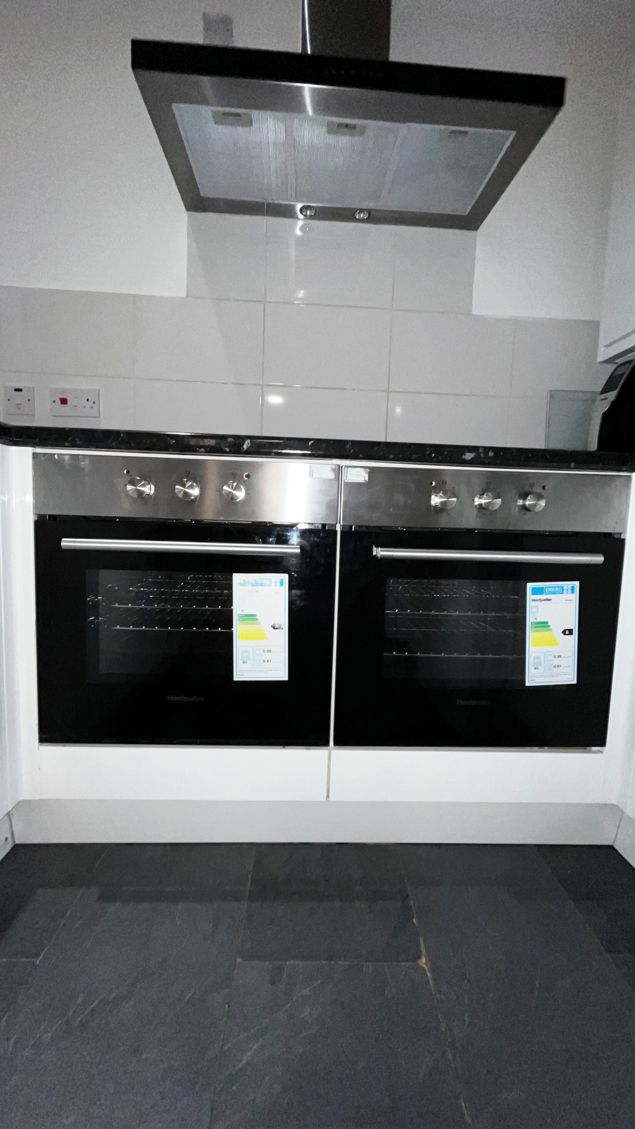 A kitchen with two stainless steel ovens, a range hood, and a tiled backsplash.