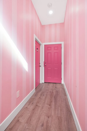 A hallway with pink walls and a wooden floor leading to a pink door. - Pretty & Pink Unit w/ Ball Pit In Philly (Philadelphia)