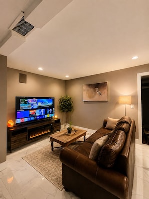 A modern living room with a flat-screen TV, leather sofa, and a decorative painting. - Ocean Park 2BR Retreat South Surrey & Parking (Surrey)