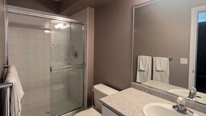 Ein Badezimmer mit einer Duschkabine, einer Toilette, einem Waschbecken mit Spiegel und einem Handtuchhalter.