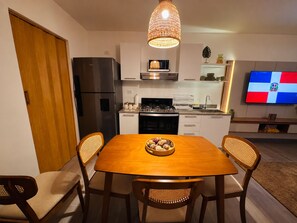 A modern kitchen with a dining table, chairs, and a television displaying a flag. - Apamate 505 • Tropical Retreat • Pool • WiFi • Near Beach (Punta Cana)