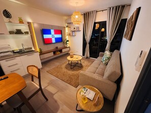 Ein modernes Wohnzimmer mit einer Couch, einem Esstisch, einem Fernseher und einer Küchenzeile.