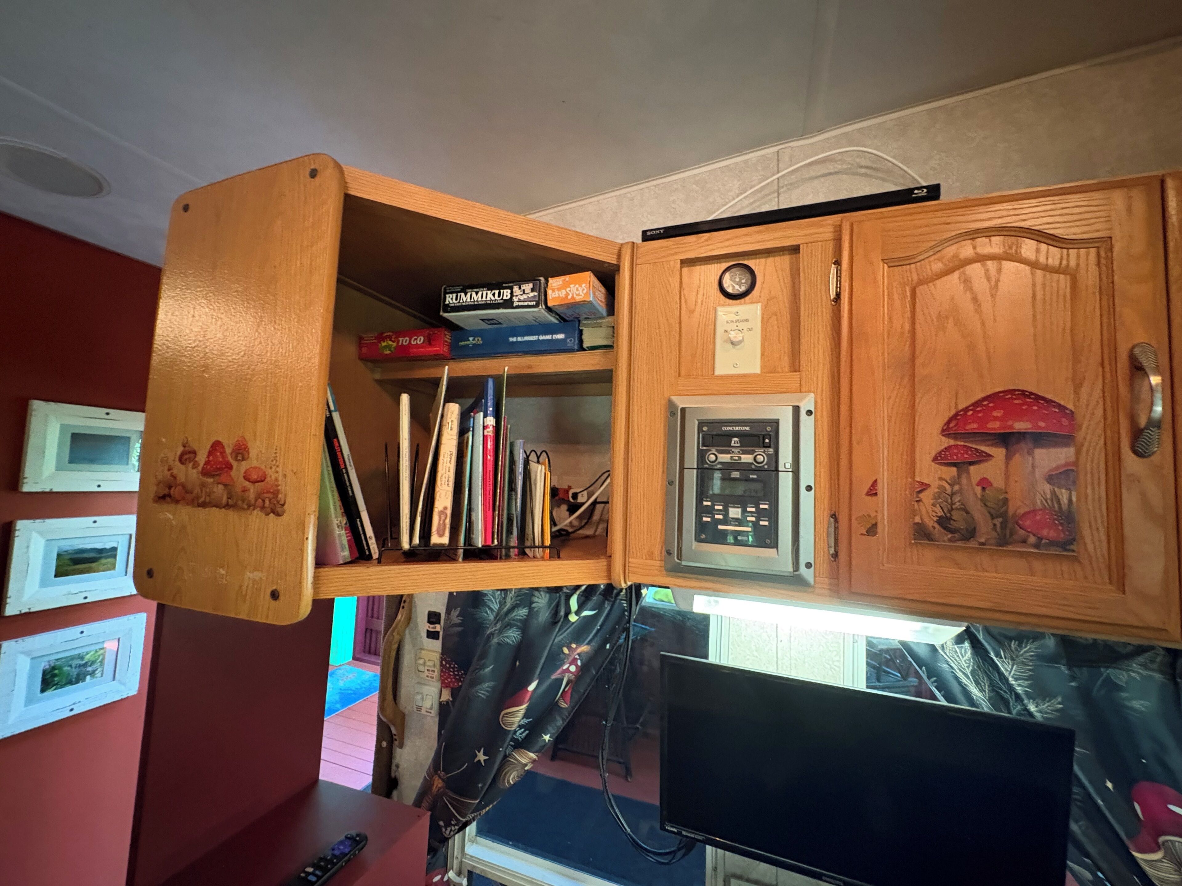 Ein Holzschrank mit einer Uhr, einem Sony-Fernseher und verschiedenen Gegenständen, darunter Bücher und einer Spielbox.