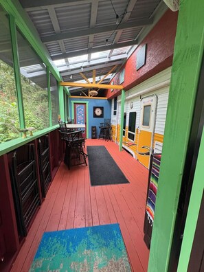 Un espace extérieur abrité comprenant une table et des chaises, un tapis noir et un mur décoré de motifs colorés sur le thème des trains.
