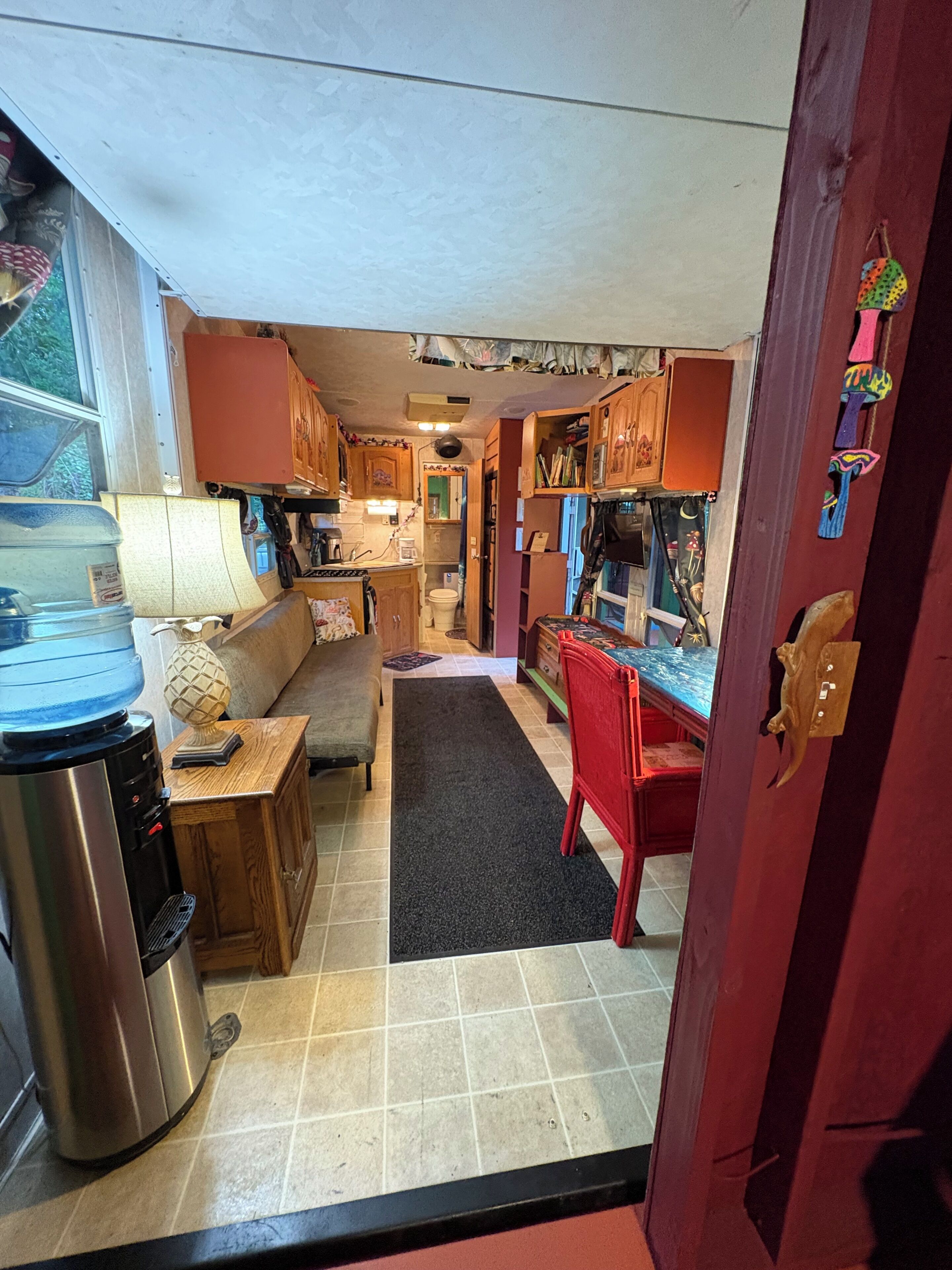A compact kitchen with a water dispenser, a coffee maker, and a red chair.