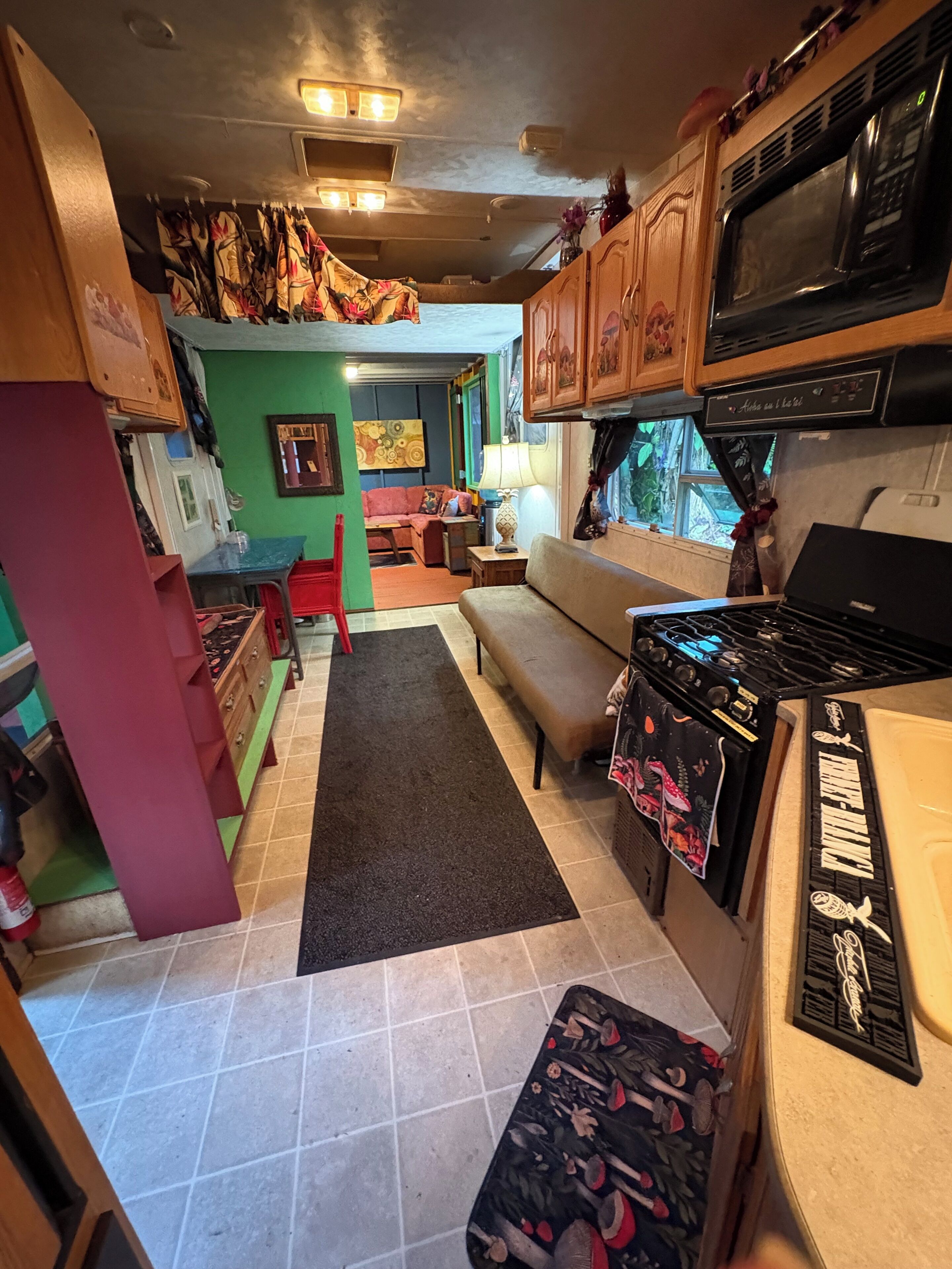 A compact kitchen with a stove, microwave, and cabinets. A sofa and a small table are placed in the living area.