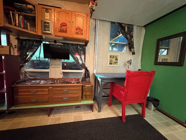 A compact room with a wooden cabinet, a small desk, a red chair, and a window with a view of a blue building.