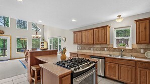 A spacious kitchen with wooden cabinets, a gas stove, a dishwasher, and a large island. - Home with access to the Elk Trail (Angel Fire)