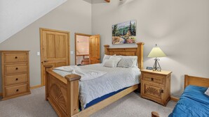 A bedroom with a wooden bed, a nightstand with a lamp, a dresser, and a painting on the wall. - Home with access to the Elk Trail (Angel Fire)