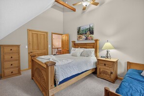 A bedroom with a wooden bed, a nightstand with a lamp, a dresser, and a painting on the wall. - Home with access to the Elk Trail (Angel Fire)