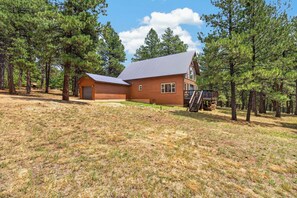 A two-story wooden cabin with a metal roof, surrounded by pine trees. - Home with access to the Elk Trail (Angel Fire)