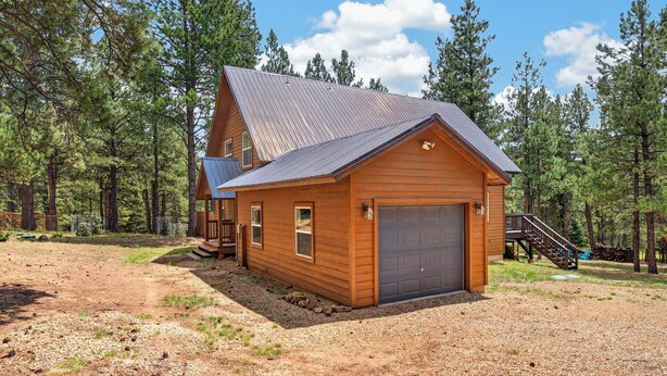 A wooden cabin with a metal roof, a garage, and a staircase leading to a deck. - Home with access to the Elk Trail (Angel Fire)