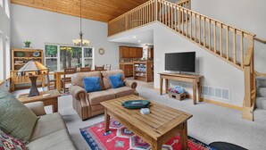 A spacious living area with a high ceiling, a wooden staircase, a television, and a cozy seating arrangement. - Home with access to the Elk Trail (Angel Fire)