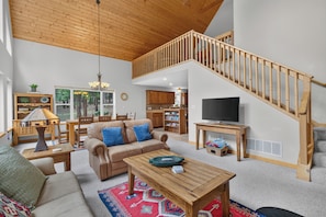 A spacious living area with a high ceiling, a wooden staircase, a television, and a cozy seating arrangement. - Home with access to the Elk Trail (Angel Fire)