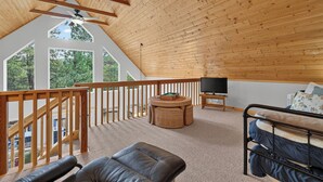 A spacious loft bedroom with a sloped ceiling, a large window offering a view of trees, a wooden ceiling, and a balcony with a view. - Home with access to the Elk Trail (Angel Fire)