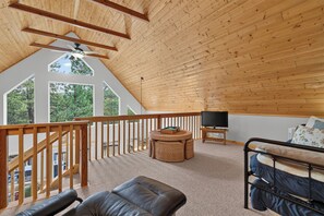 A spacious loft bedroom with a sloped ceiling, a large window offering a view of trees, a wooden ceiling, and a balcony with a view. - Home with access to the Elk Trail (Angel Fire)