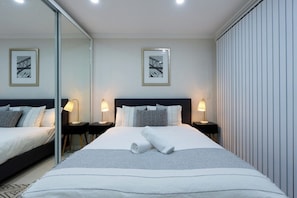 Ein Hotelzimmer mit einem großen Bett, zwei Nachttischen mit Lampen, einem Spiegel und zwei gerahmten Bildern an der Wand.