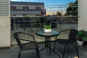 An outdoor seating area with two chairs and a table, a potted plant, and a view of a building with a sign for 'BONDS OUTLET'.