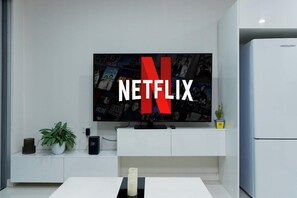 A modern living room with a flat-screen TV displaying the Netflix logo, a white cabinet, a potted plant, and a white refrigerator.