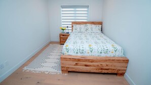 A bedroom with a wooden bed, a nightstand, a window with blinds, and a patterned rug.