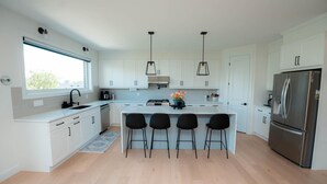 A modern kitchen with white cabinetry, a central island with bar stools, a stainless steel refrigerator, and pendant lighting.