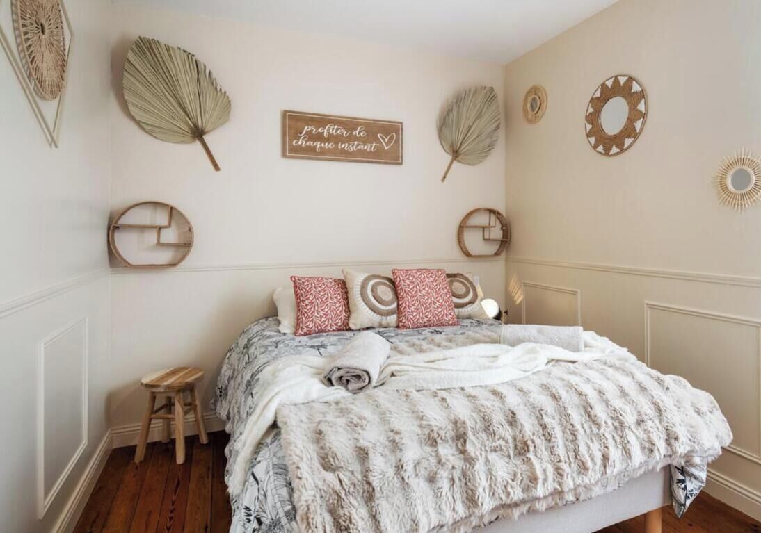 Ein Schlafzimmer mit einem Bett, Kissen, einem kleinen Hocker und Wanddekorationen, darunter Blätter und ein Schild.