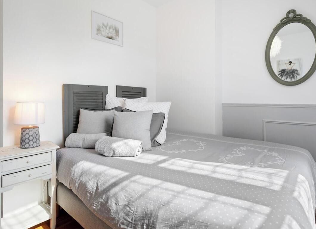 Una camera da letto con un letto, un comodino, una lampada, uno specchio e un quadro appeso al muro.