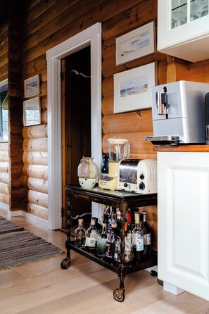 A wooden cabin interior with a kitchen area featuring a toaster, a blender, and a cart with bottles. - Traditional cabin among the dunes (Skagen)