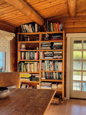 A wooden bookshelf filled with books in a room with wooden walls and a window. - Traditional cabin among the dunes (Skagen)