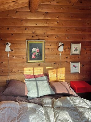 A cozy bedroom with a wooden ceiling, a bed with multiple pillows, and wall-mounted lamps. - Traditional cabin among the dunes (Skagen)