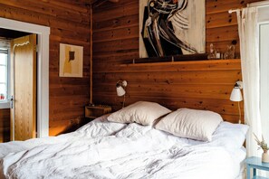 A wooden room with a bed, two bedside lamps, a painting, and a window with curtains. - Traditional cabin among the dunes (Skagen)