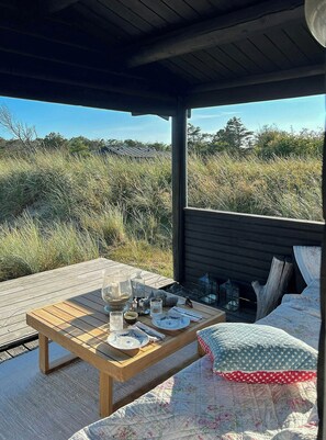 A covered outdoor seating area with a table set for dining, overlooking a natural landscape. - Traditional cabin among the dunes (Skagen)