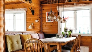A wooden cabin interior with a dining table surrounded by chairs, a bench, and a window with curtains. - Traditional cabin among the dunes (Skagen)