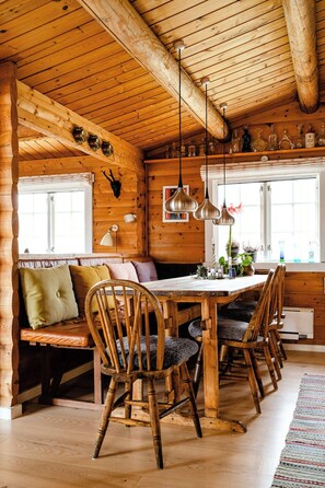 A wooden cabin interior with a dining table surrounded by chairs, a bench, and a window with curtains. - Traditional cabin among the dunes (Skagen)