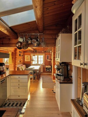 Cocina acogedora estilo cabaña con vigas de madera, zona de comedor con mesa y sillas, y un ventanal que proporciona luz natural.