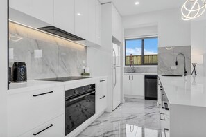 A modern kitchen with white cabinetry, a black oven, and a marble backsplash. - Modern Sunbury Home – Mins to Rupertswood (Sunbury)