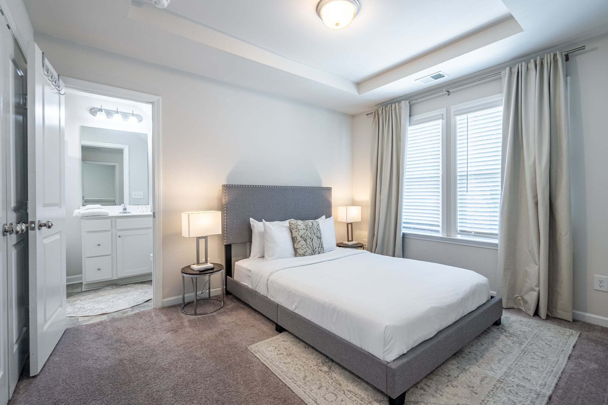 A hotel room with a bed, bedside lamps, a mirror, and a window with curtains.
