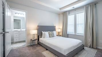 A hotel room with a bed, bedside lamps, a mirror, and a window with curtains.